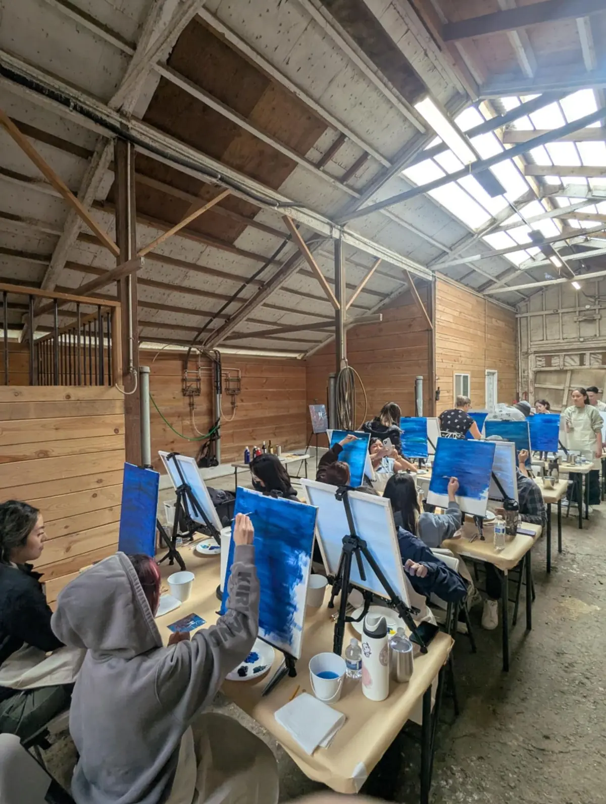 Rows of guests painting blue skies on their canvases in the barn