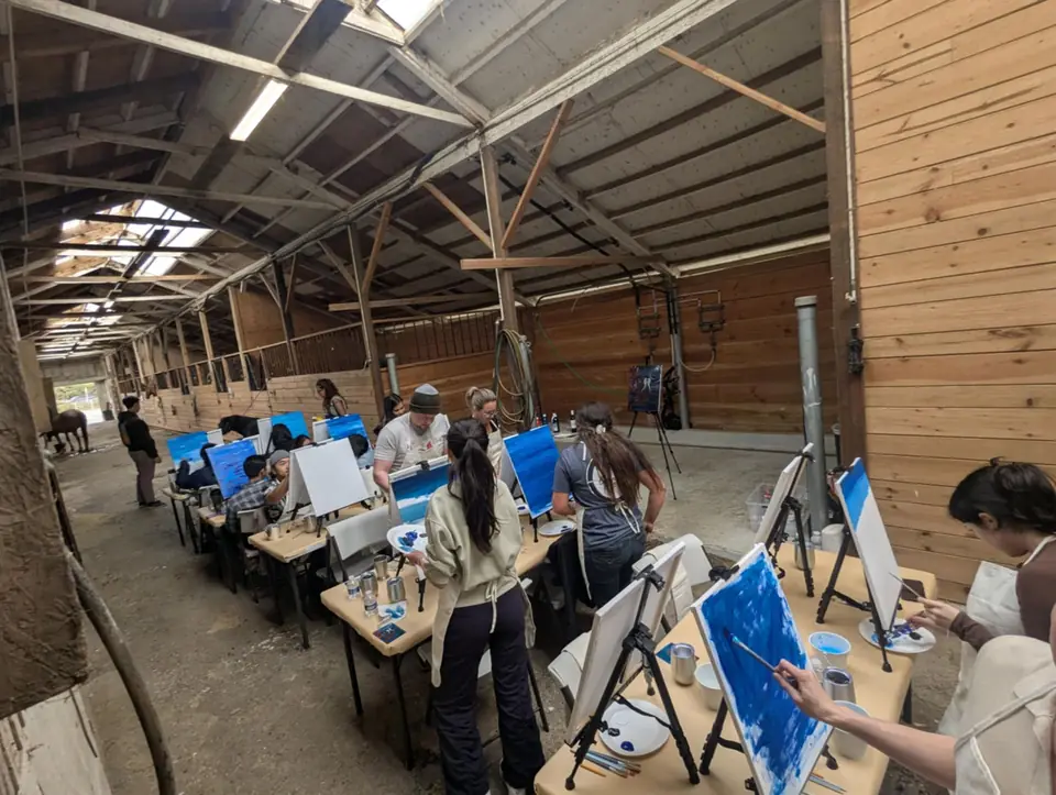 Guests painting at long tables down the barn aisle at Ocean View Stables, canvases on easels