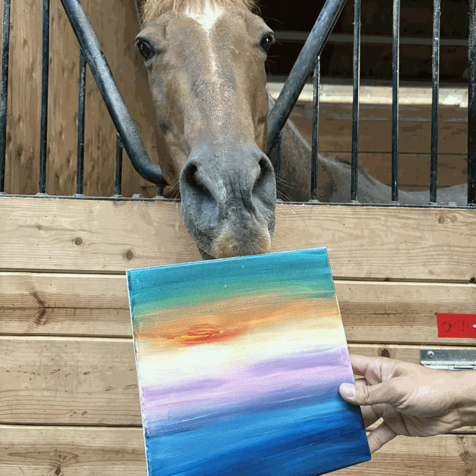 A horse looking over its stall door at a guest's freshly painted sunset canvas