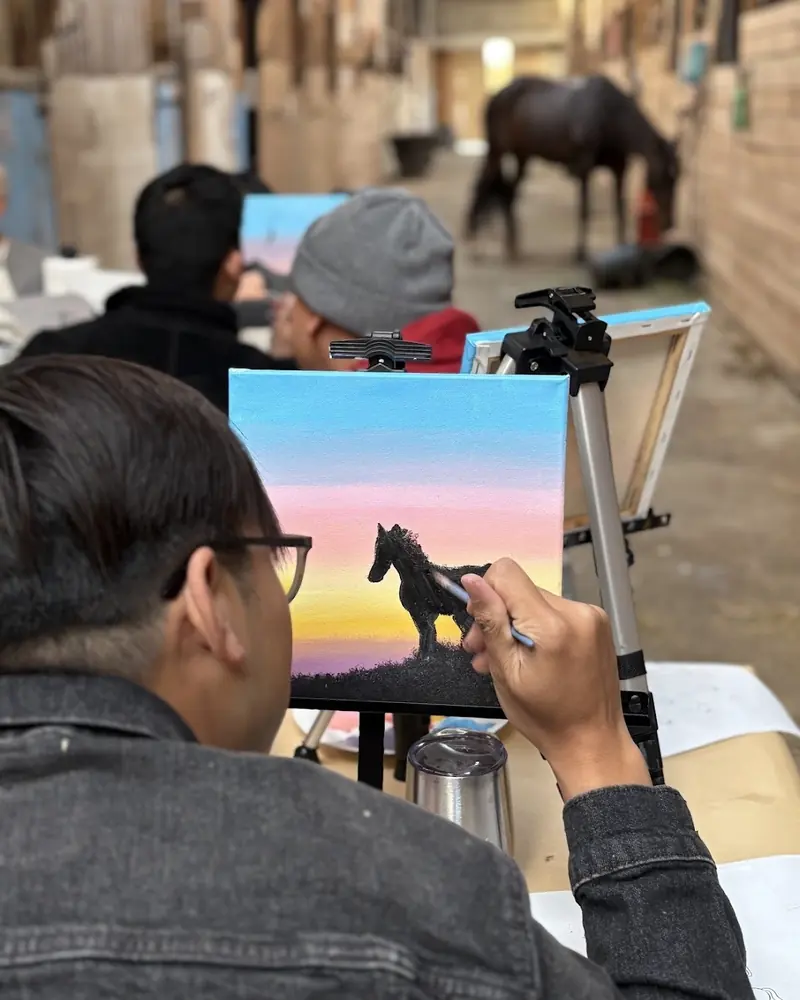 A guest painting a horse silhouette against a sunset sky, following the session's sample canvas